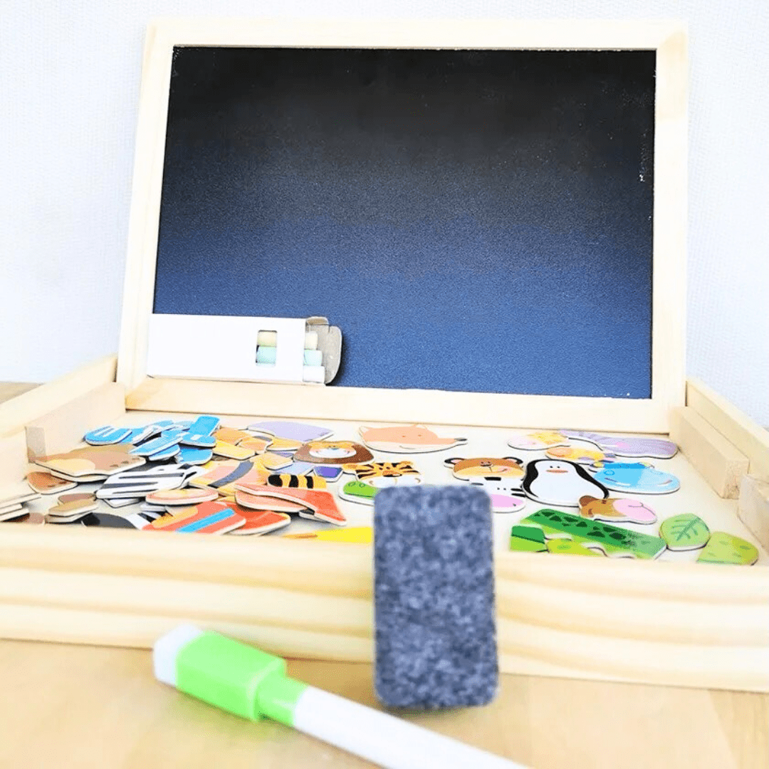 Tableau noir magnétique pour enfant ouvert sur une table, avec une grande variété de pièces magnétiques en bois et un feutre effaçable.