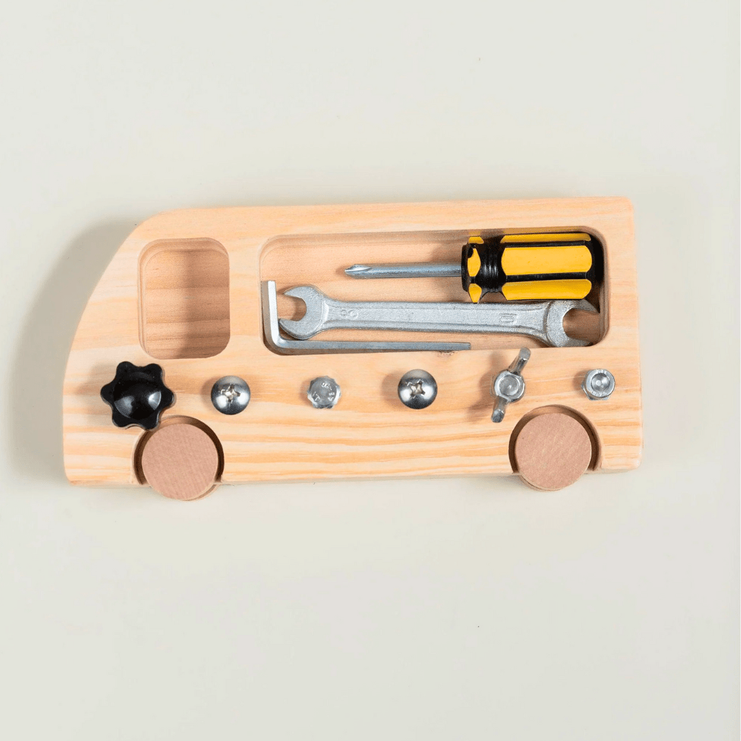 présente un jouet en bois clair en forme de véhicule avec des roues en bois. Il comporte des compartiments intégrés contenant de petits outils : un tournevis à manche jaune et noir, une clé plate métallique, et une clé Allen. Le jouet est aussi équipé de plusieurs vis et écrous métalliques ainsi qu'un bouton noir en forme d'étoile fixés sur la surface.