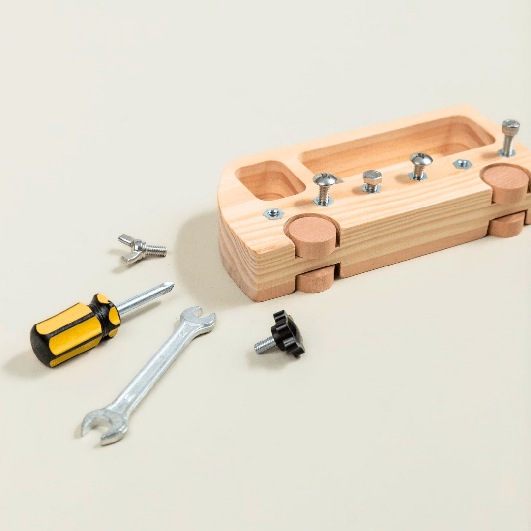 présente une autre vue du jouet où l'on voit la base en bois du véhicule avec ses compartiments, ainsi que les différents outils et fixations placés à côté. Cette vue montre bien que ce jouet est conçu comme un jeu éducatif pour développer la motricité et la compréhension mécanique.