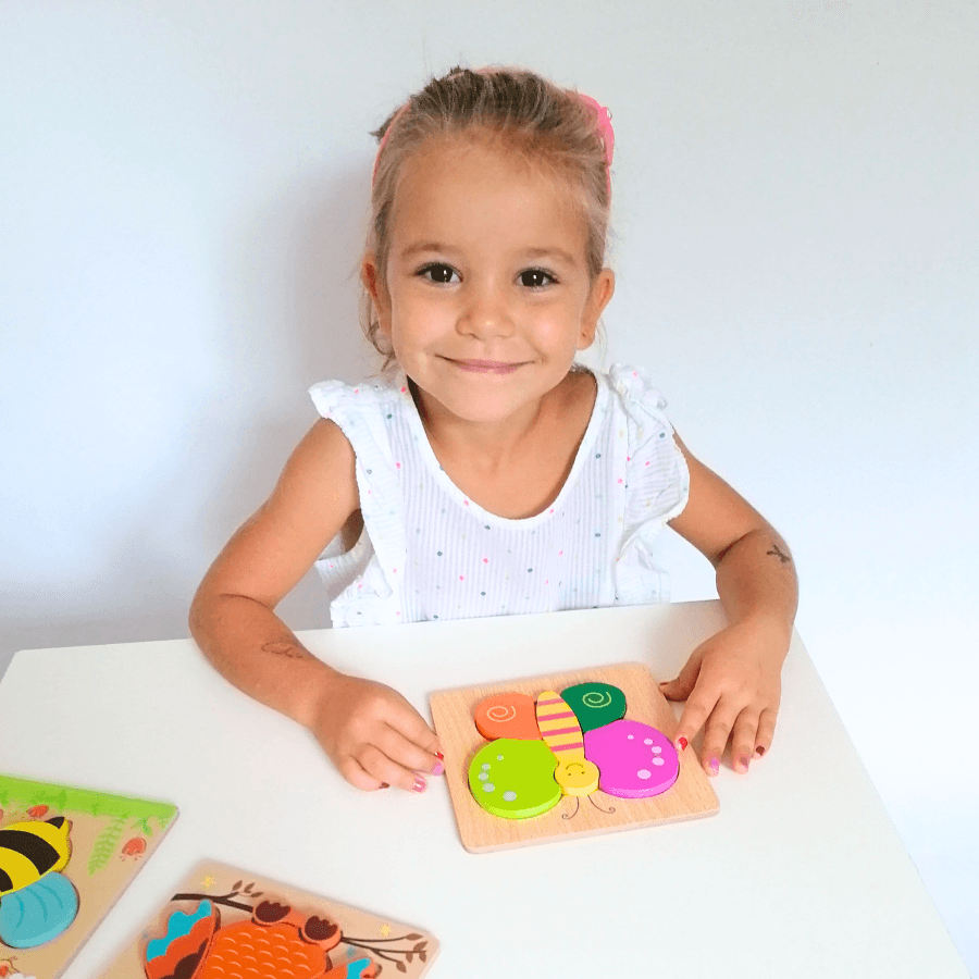 Petite fille souriante qui assemble un puzzle papillon en bois