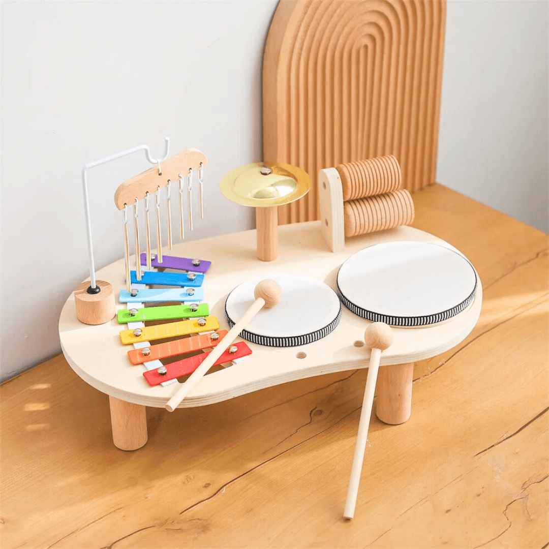 Kit musical Montessori en bois pour enfant avec tambours, xylophone coloré, cymbale et barres sonores, posé sur une table en bois clair.