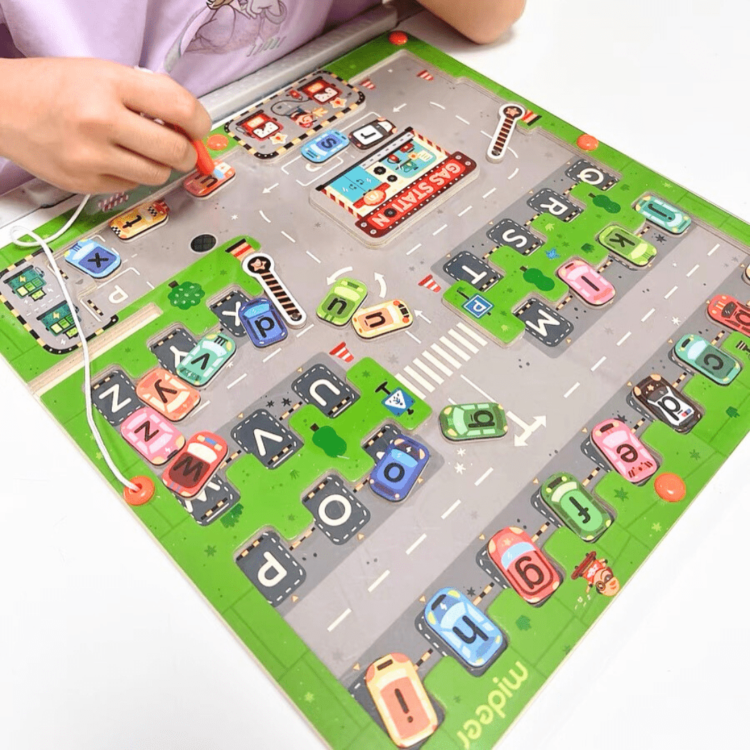 Jeu éducatif Montessori avec un enfant utilisant un stylet magnétique pour déplacer des voitures-lettres sur un circuit ludique représentant l'alphabet.