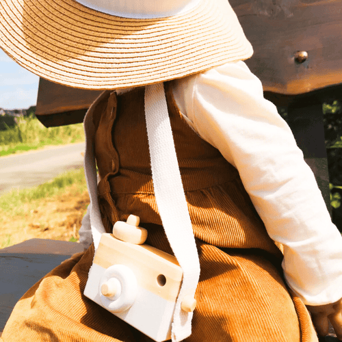 Appareil photo en bois porté par un enfant dans l’herbe, illustrant un jouet Montessori pour stimuler l'imagination et le jeu en plein air