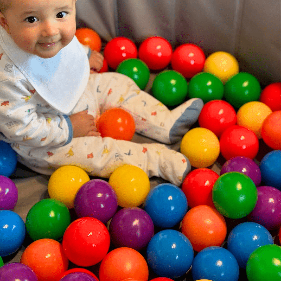 Bébé assis dans une piscine remplie de balles colorées, jouant avec des balles sensorimotrices pour stimuler la motricité et l’éveil visuel.