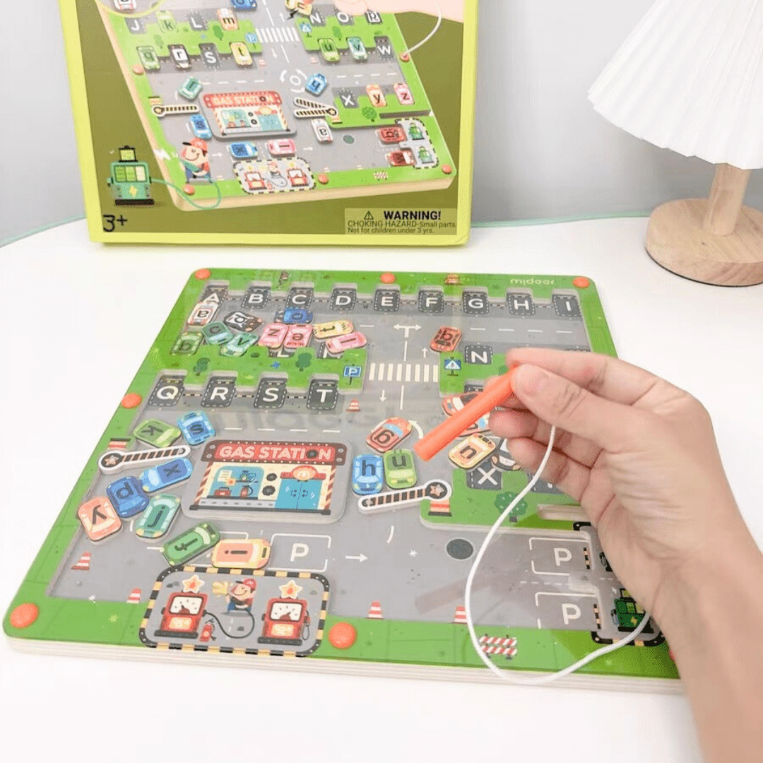 Main tenant un stylet magnétique au-dessus du busy board en bois, montrant les lettres dispersées sur le plateau en forme de route.