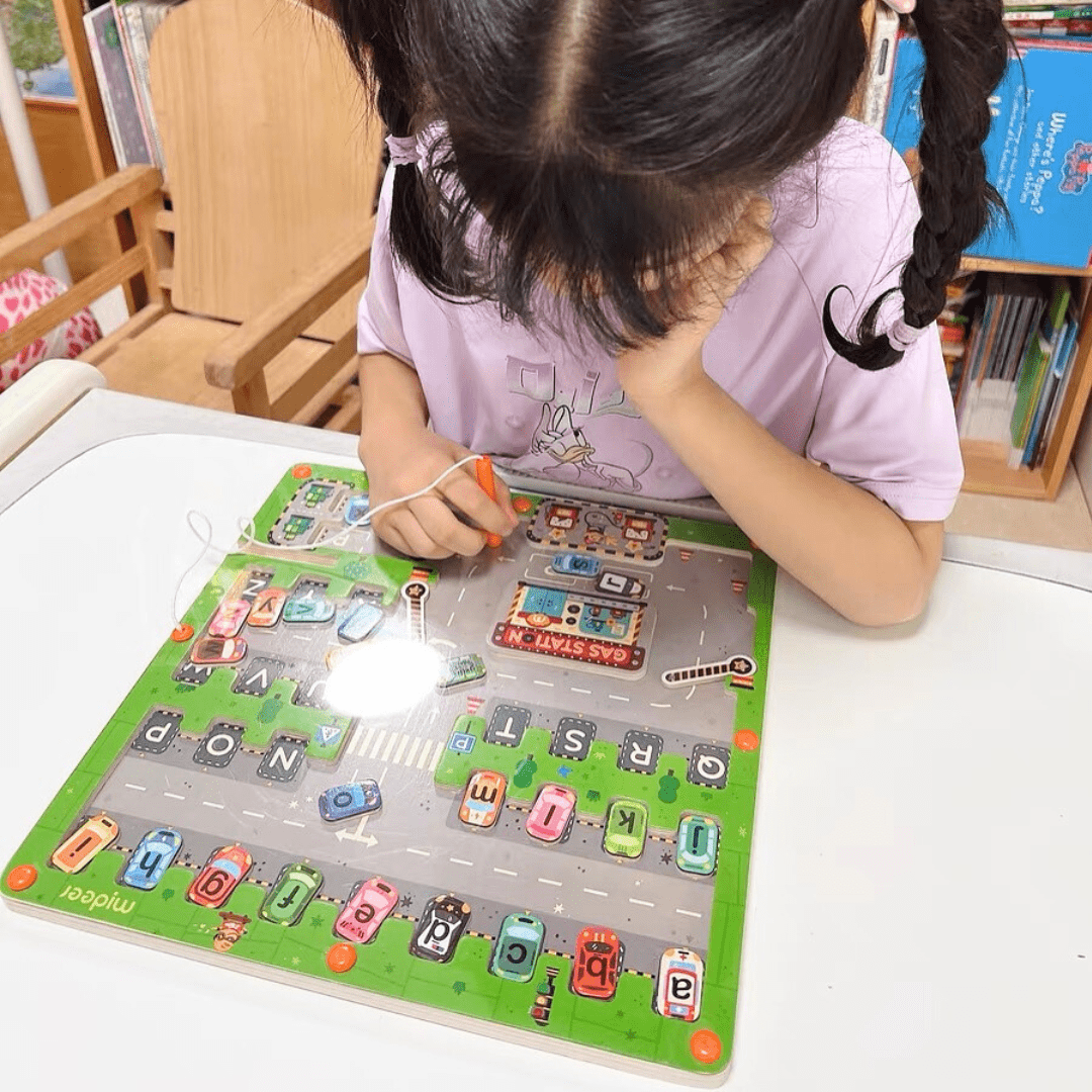 Petite fille concentrée manipulant le jeu de lettres aimantées Montessori sur une table blanche, dans un environnement éducatif.