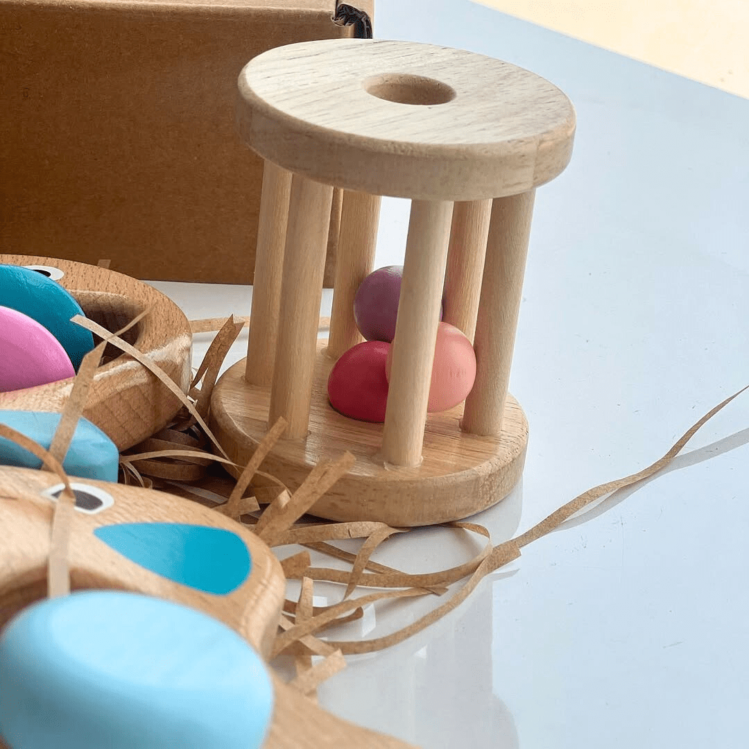 hochet avec 3 petites balles colorée et un carton d'emballage en arrière plan.